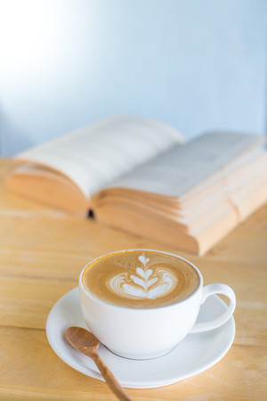 Latte art coffee with open book on wood table in coffee shopの写真素材