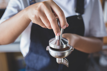 Lady barista holding a coffee portafilter with ground coffee and is about to press it with the tamper.の写真素材