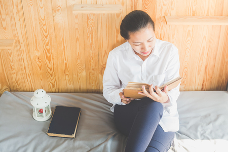 Soft image of young Asain woman reading book on her bed in bedroomの写真素材