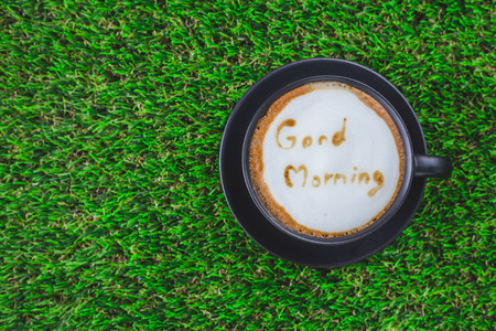 A cup of coffee capuccino with wording  Good Moring   in black cup on grass