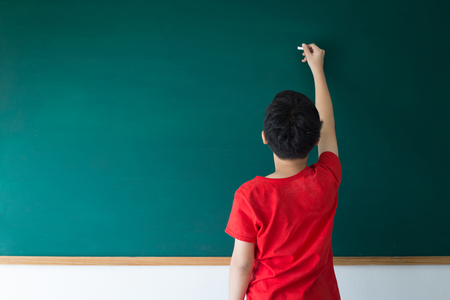 Asian boy writing on empty green board in class room at schoolの写真素材