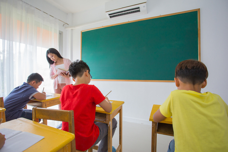 Group of school kids with pens and notebooks studying in classroom with teacher