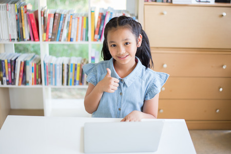 Girl with laptop in library and showing thumb upの写真素材
