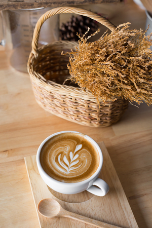 A cup of coffee latte with dried flower in basket on wood table.の写真素材