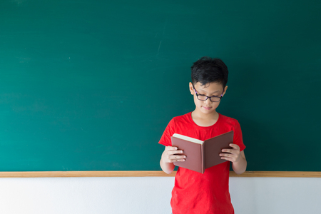 Portrait Asian children boy reading near blank chalkboard in schoolの写真素材