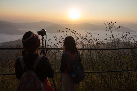 Silhouette womans and  shooting camera sunset on the top mountain. Relax time travel on holiday