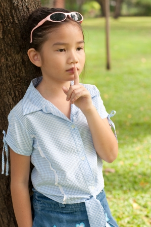 Portrait of beautiful little asian girl in the park,  she make finger on lips, Thailand.の写真素材