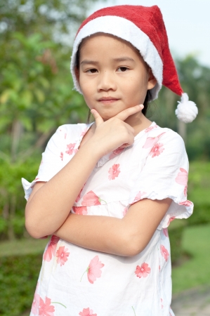 Portrait of lovely asian girl in white suit and Santa hat at public park, Thailand.の写真素材
