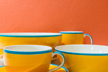 Bowls, plate  and cups with orange wall and white floor, Thailand.の写真素材