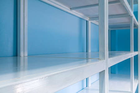 Empty white shelves in blue storage room, focus at front shelfの写真素材