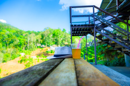 Iced tea in plastic glass and white cloth hat on wooden table in high mountain farm with natural view at Chiang Mai Province, Thailand.の写真素材