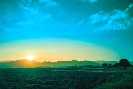 Landscape Series : Silhouette view of a mountain range with pagoda on top during sunset. Rural view of Chiang Rai province, Thailand. Beautiful evening atmosphere of rice fields and twilight sky.の写真素材