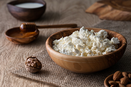 Cottage cheese in a wooden bowl on a textured wooden surface, close up view