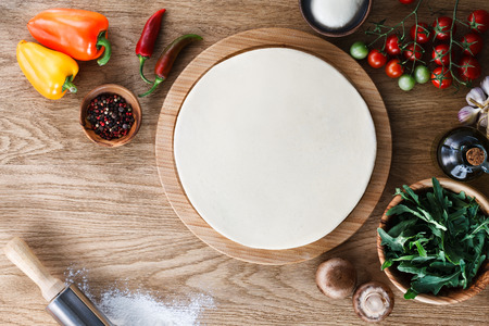 Fresh dough pizza base  and ingredients on a wooden textured table. Top view.の写真素材