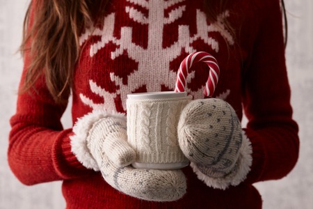 Woman hands in cute christmas mittens holding a cup of coffee or cocoa with a candy caneの写真素材