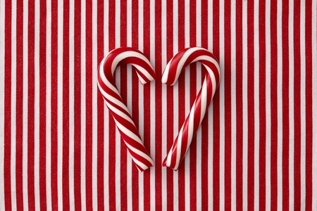 Striped peppermint candy canes in heart shape on a striped textile backgroundの写真素材