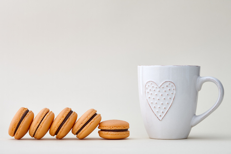Orange French macarons and a white cup with heart on a beige backgroundの写真素材