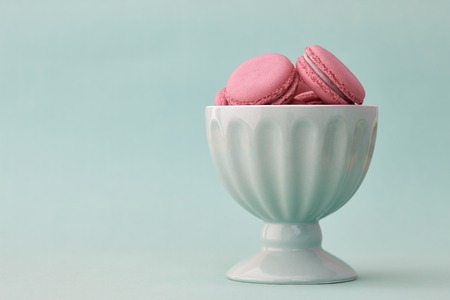 Pink French macarons in a turquoise bowl on a turquoise backgroundの写真素材