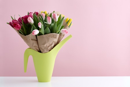 Pink and violet spring tulips bouquet in a light green watering can on a pink backgroundの写真素材