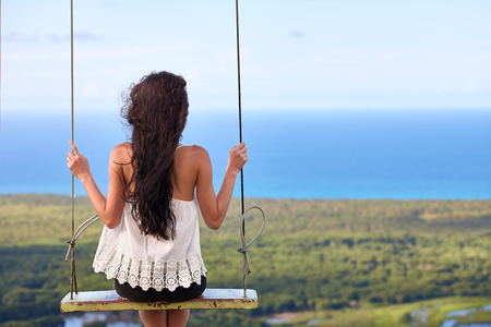 Woman on a swing in the mountains watching a beautiful sea landscapeの写真素材