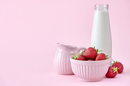 A food background with a bowl full of fresh strawberries, milk bottle and milk jar. Pink colors.の写真素材