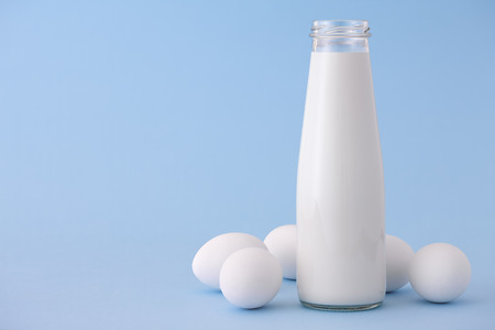 Bottle of milk and white eggs on a blue backgroundの写真素材