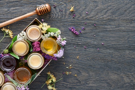 A box with eight different kinds of honey decorated with blossoms of bee plants. Top view.