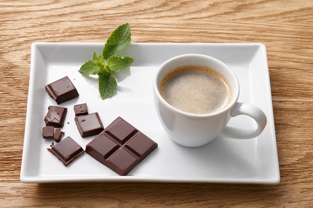 Espresso coffee and pieces of dark chocolate on white rectangular plate, wooden backgroundの写真素材