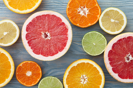 A mix of different citrus fruits cut in half, blue wooden backgroundの写真素材