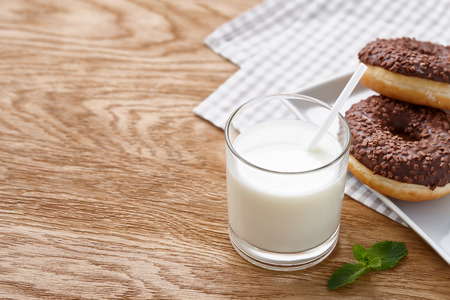 A glass of milk and glazed chocolate donuts on wooden tableの写真素材