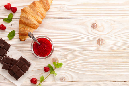 Morning breakfast with raspberry jam, fresh croissant and chocolate bar.