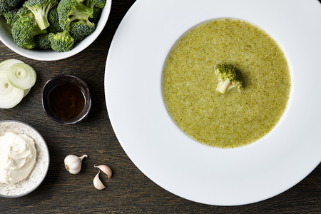 White plate with broccoli soup and ingredients on dark wooden backgroundの写真素材
