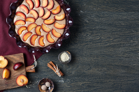 Plum pie cooking process. Pie dish with dough and fruit pieces on dark backgroundの写真素材