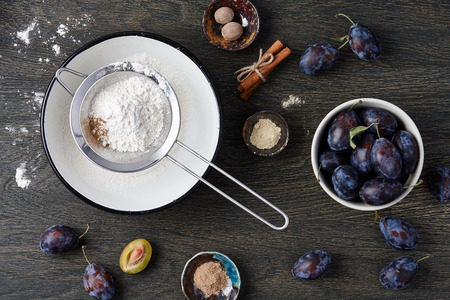 Plum pie cooking process. Powdered sugar, plum fruits and spices on dark wooden background.の写真素材