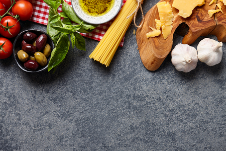 Italian food ingredients stone background with raw spaghetti, olives, basil leaves, parmesan cheese, garlic, olive oil and tomatoes.の写真素材