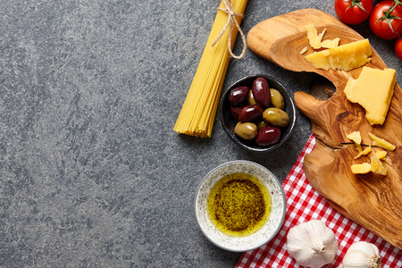 Italian food ingredients stone background with raw spaghetti, olives, parmesan cheese, garlic, olive oil and tomatoes.の写真素材