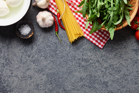 Italian food ingredients background with raw spaghetti, rocket salad, mozzarella cheese, chili pepper, garlic, salt and tomatoes.の写真素材
