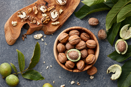 Wooden bowl with fresh walnuts, leaves and nut shell on gray stone background. Autumn seasonal.の写真素材