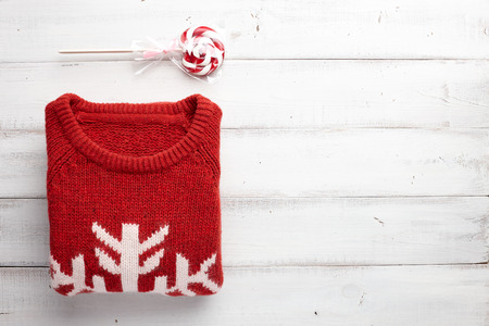 Winter holiday knitted sweater and christmas lollipop on white wooden background.
