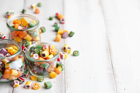 Glass jars with colorful sugar candies on white wooden background