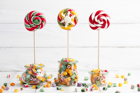 Colorful lollipops and candy canes in glass jars on white wooden backgroundの写真素材