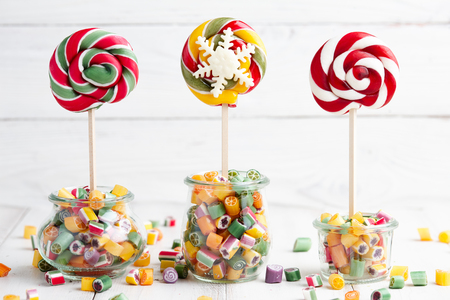 Colorful lollipops and candy canes in glass jars on white wooden backgroundの写真素材