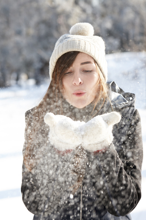Young woman blowing snowflakes off her handsの写真素材