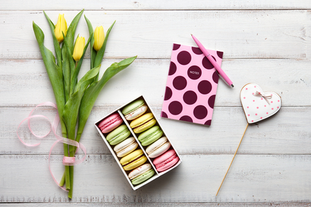 Working place. Macarons, gingerbread, flowers and notebook with pen on white wooden boardsの写真素材