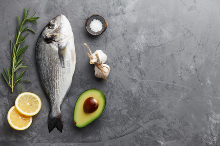 Fresh dorado or gilthead bream cooking with rosemary, avocado, garlic, lemon and salt on stone backgroundの写真素材