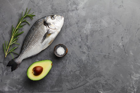Fresh dorado or gilthead bream cooking with rosemary, avocado, garlic and salt on stone backgroundの写真素材