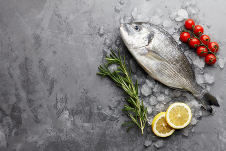 Fresh dorado or gilthead bream cooking with rosemary, cherry tomatoes and lemon on stone backgroundの写真素材