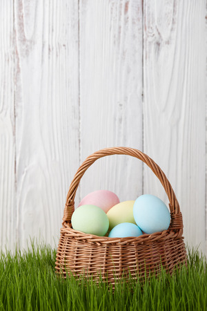 Colorful easter eggs basket in a grass meadow on white fence backgroundの写真素材