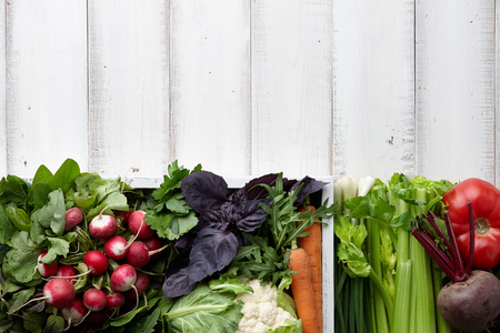 Fresh vegetables and herbs in wooden box on white table, copyspaceの写真素材