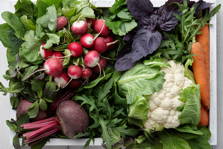Fresh vegetables and herbs in wooden box on white table, top viewの写真素材